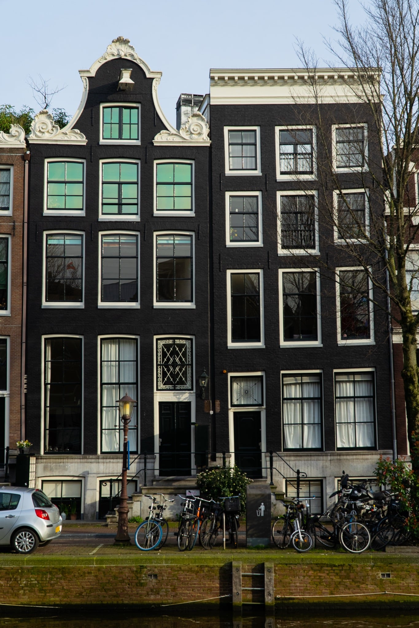 Grand black-brick canal houses with an ornate white gable and a street lamp along the water