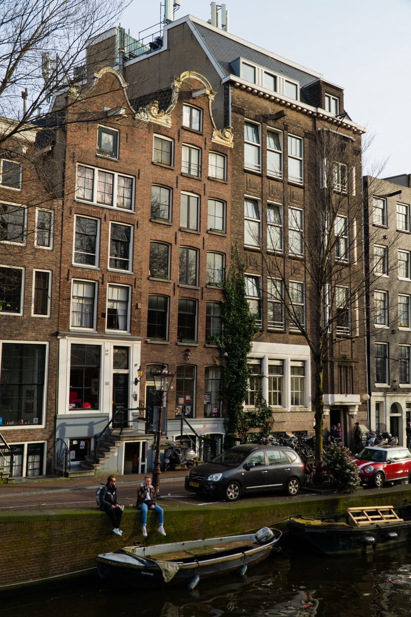 A scrolled Baroque gable atop a tall brick canal house, two young men resting on the quay below