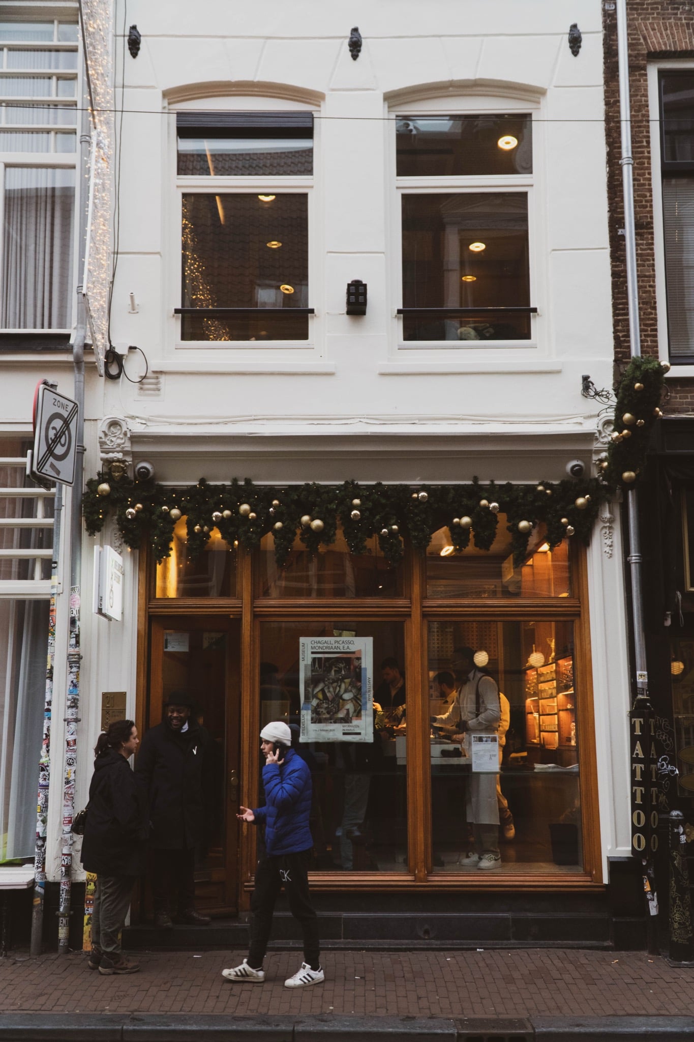 A festively garlanded shopfront on a narrow street, its window advertising a Chagall–Picasso–Mondrian exhibition