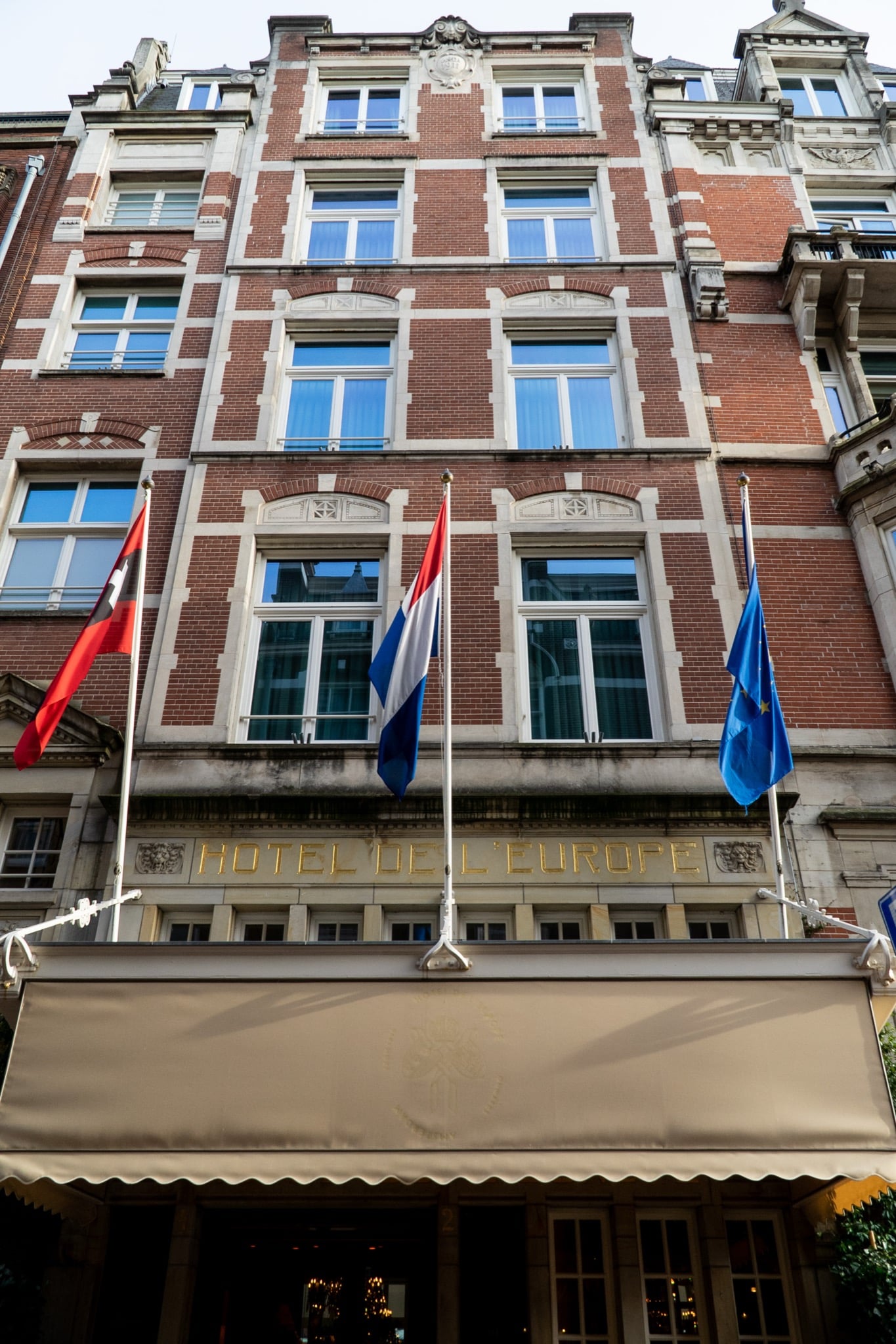 The red-brick facade of the Hotel de l'Europe flying the Amsterdam, Dutch and EU flags