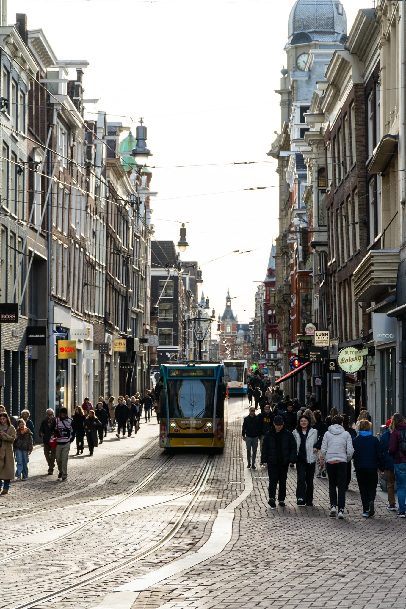 A yellow tram threading crowds down the Leidsestraat shopping street at golden hour