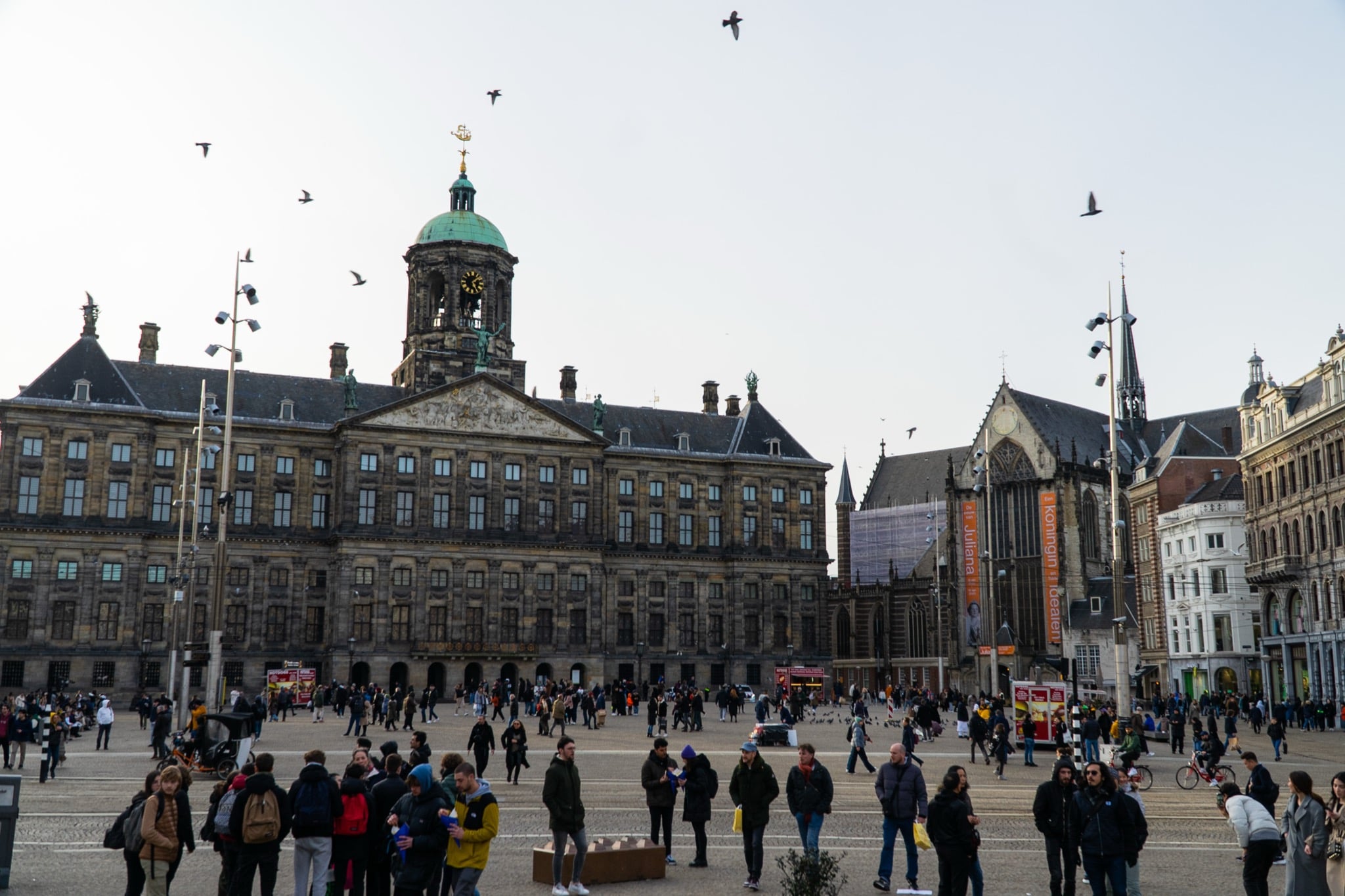 The Royal Palace and Nieuwe Kerk overlooking a crowded Dam Square with pigeons in flight