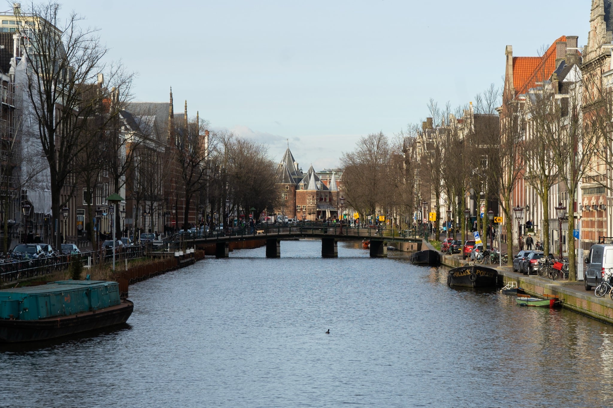 A broad canal curving toward the turreted Waag, houseboats moored along the quays