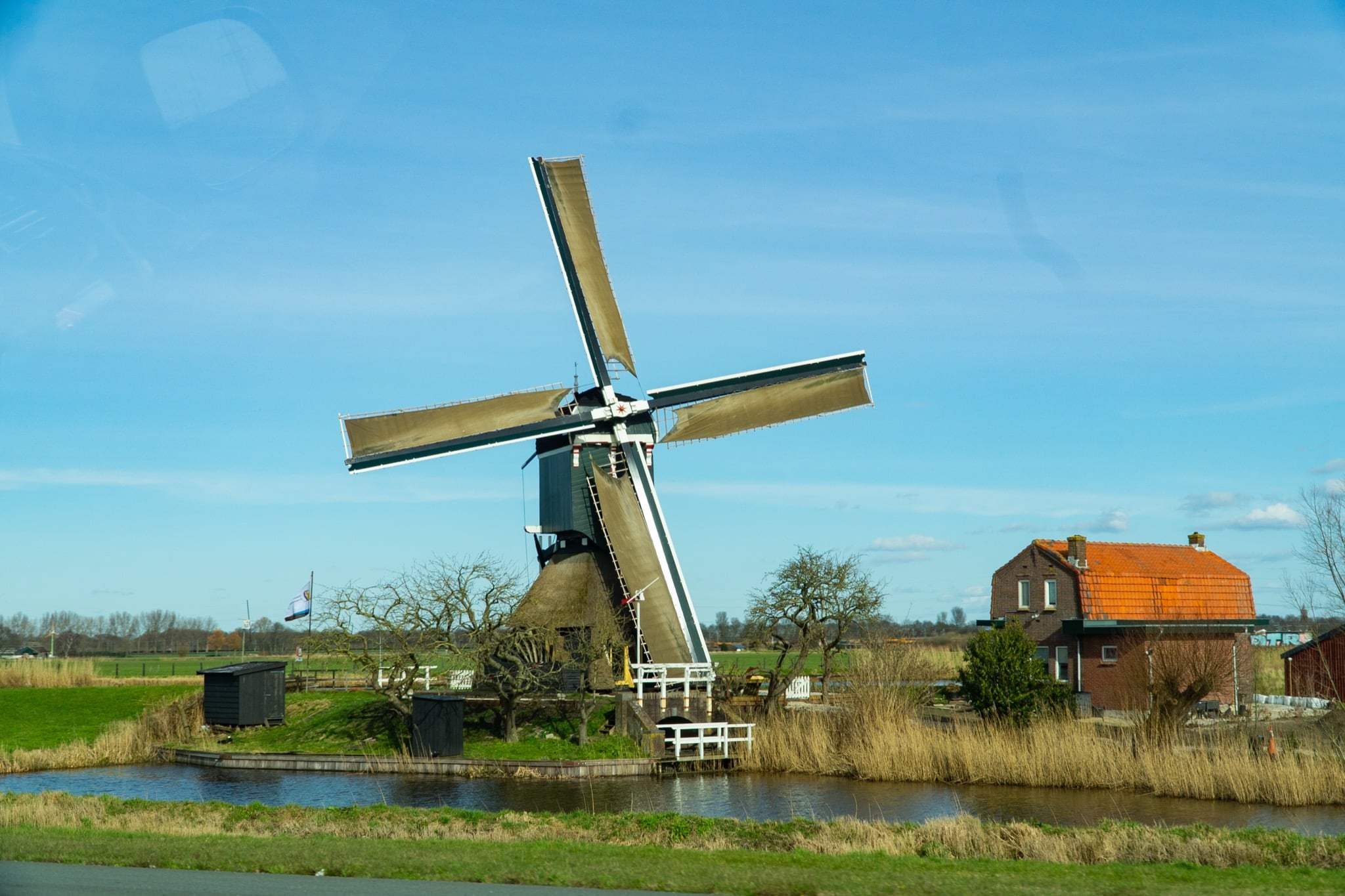 A traditional Dutch windmill beside a canal in the polder, a red-roofed farmhouse alongside