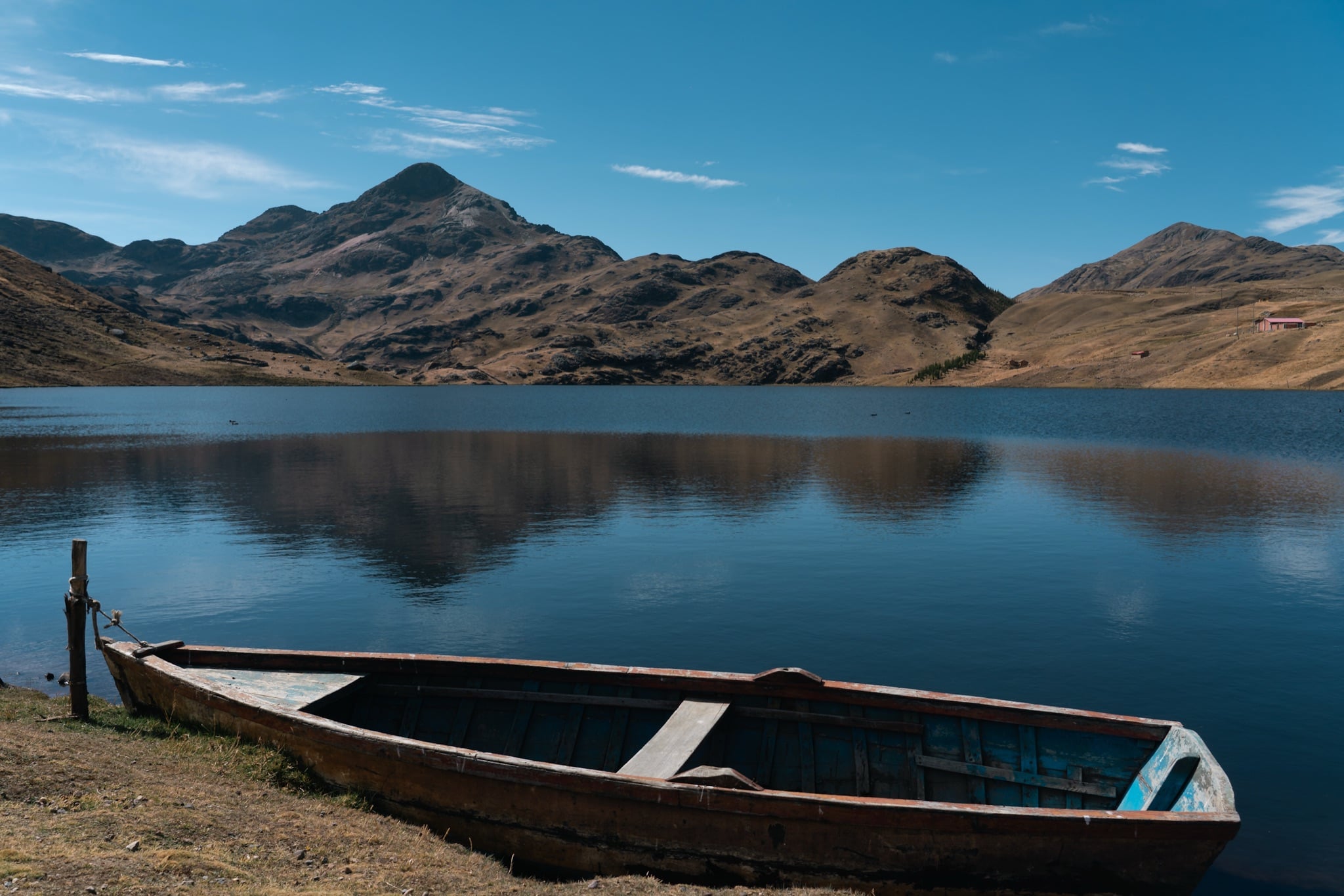 A wooden boat resting on the shore of a still Andean lake