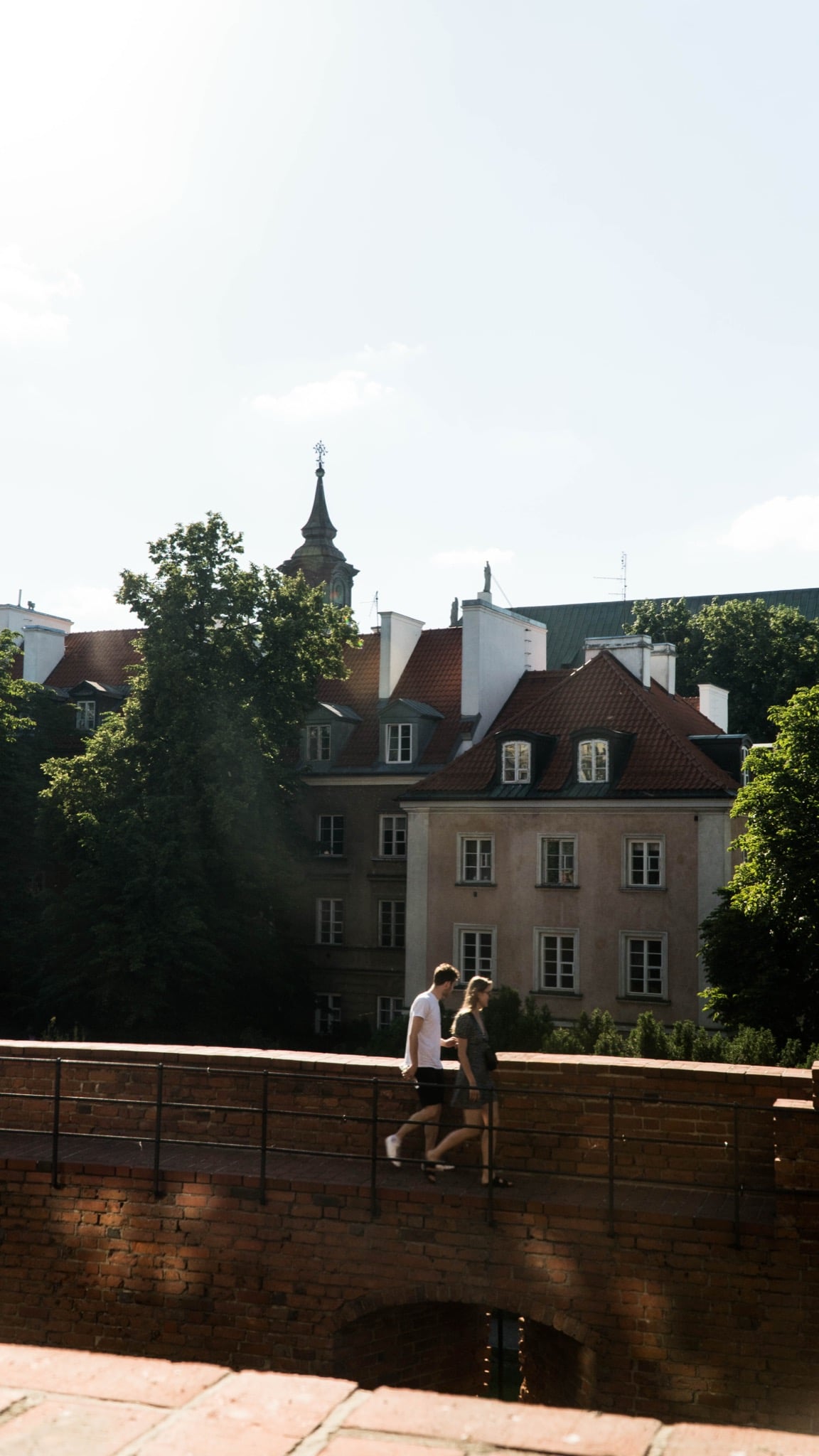 A couple strolling along the brick Barbican wall, red-roofed Old Town houses behind