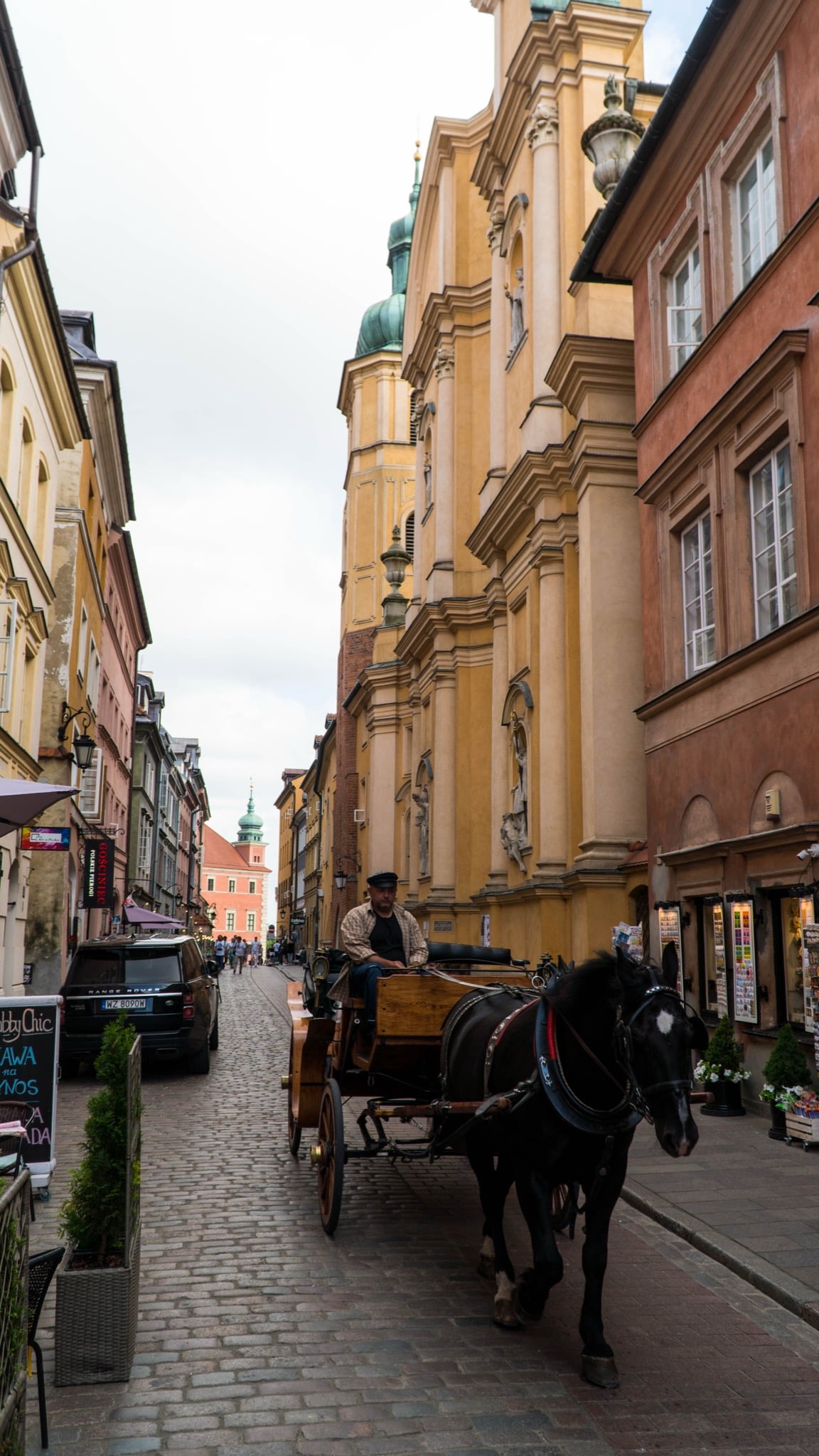A horse-drawn carriage on a cobbled Old Town lane beside a Baroque church, the Royal Castle tower beyond