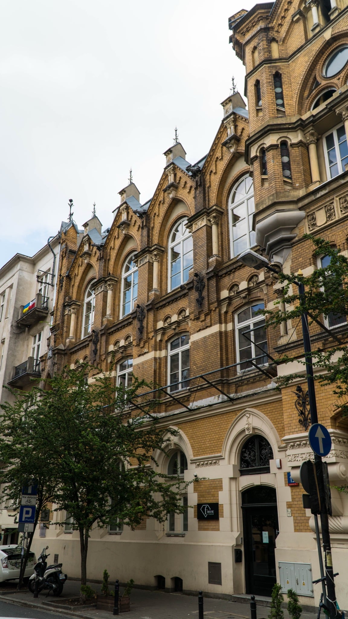 An ornate yellow-brick Neo-Gothic facade with gabled windows on a Warsaw street