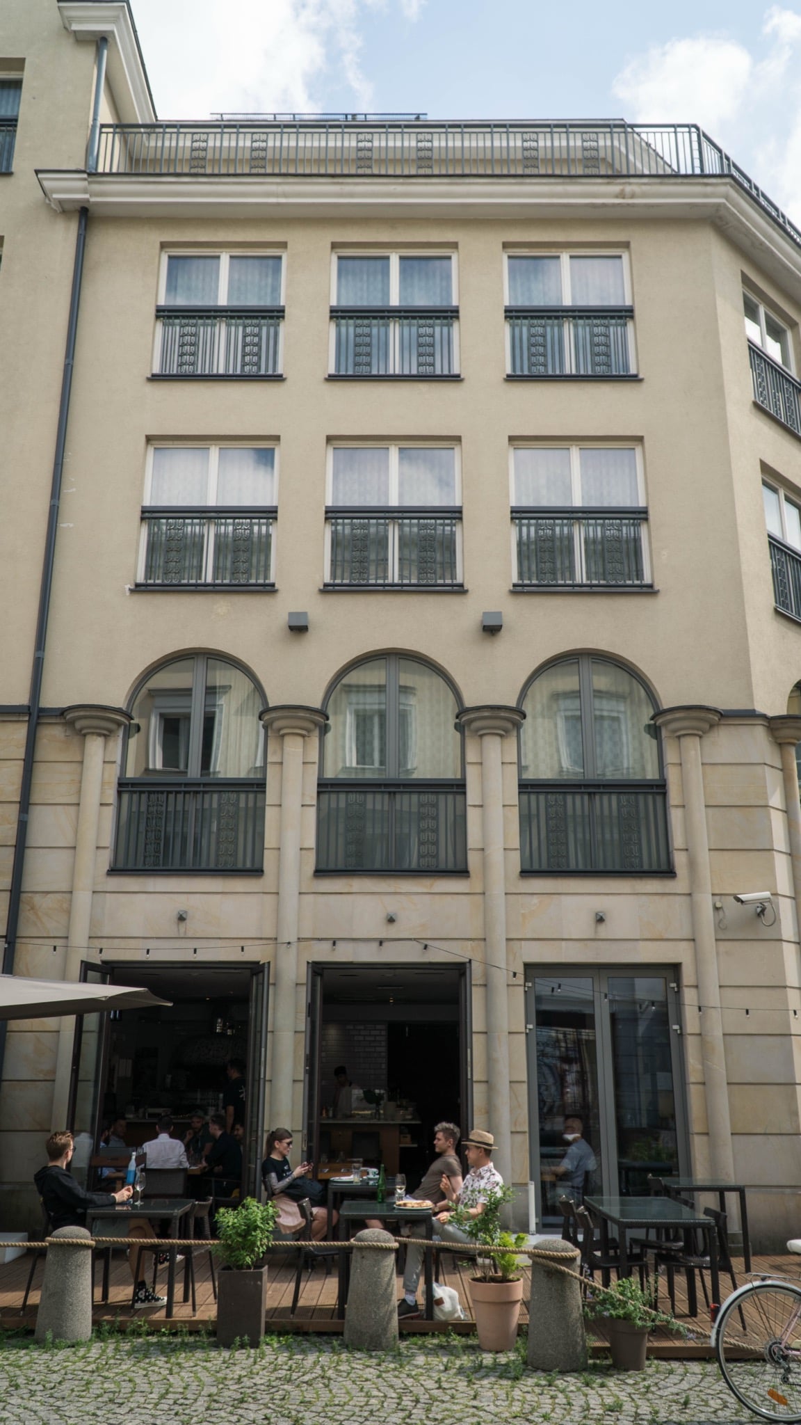 Diners at an outdoor café beneath the arched windows of an elegant restored Warsaw townhouse