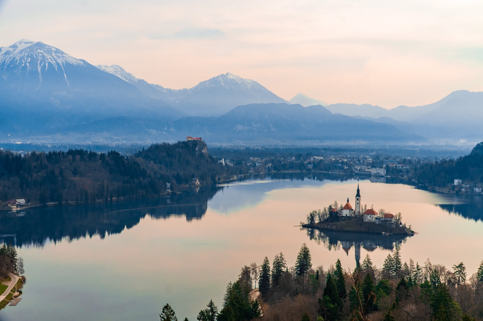 Lake Bled at first light, the island and mountains reflected under a pastel sky