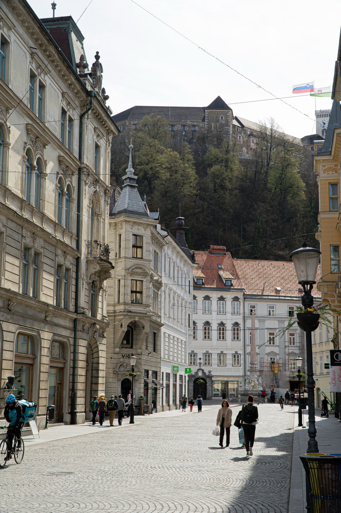 A cobbled old-town street below the castle hill, a cyclist passing, Ljubljana