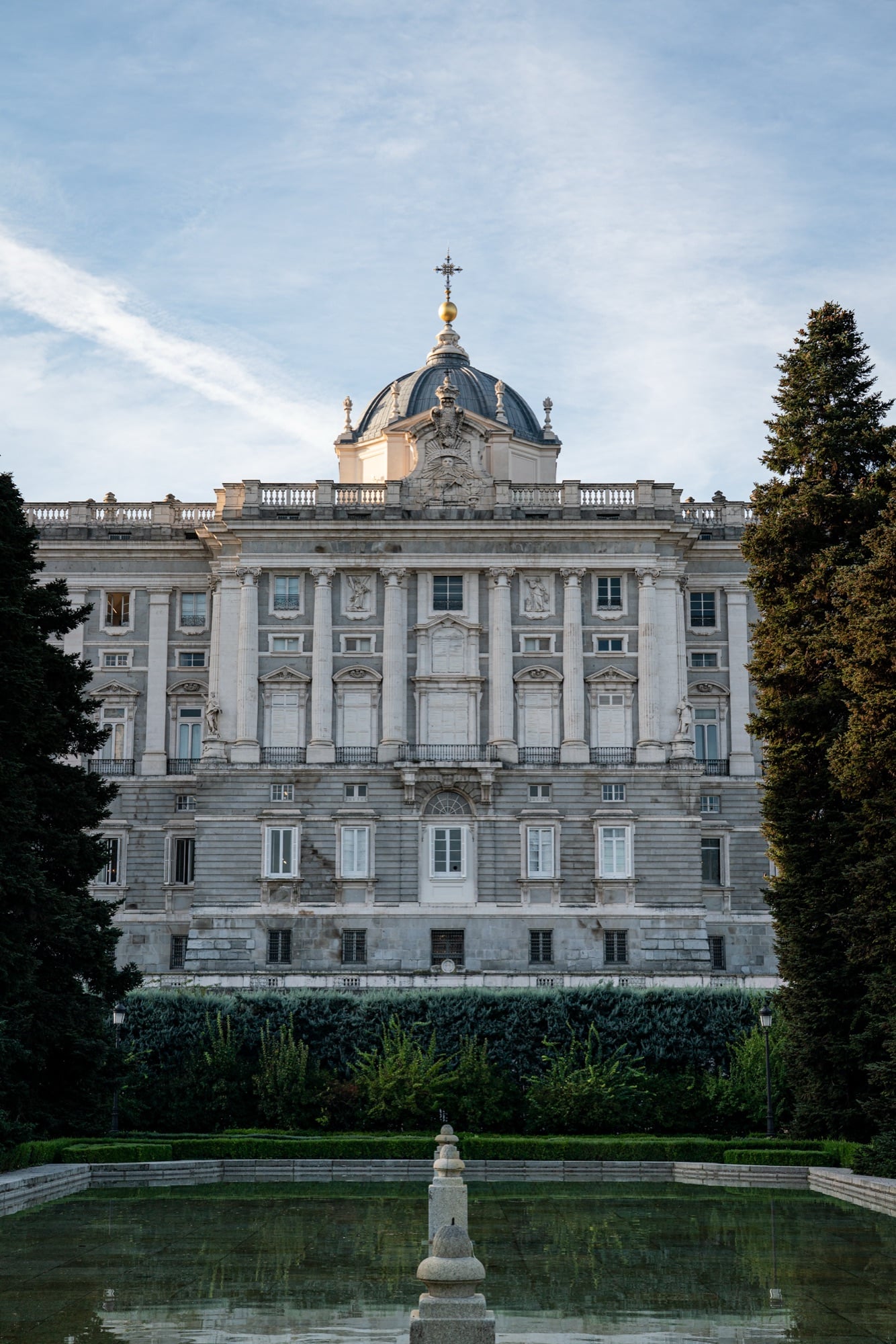 The north facade and dome of the Royal Palace framed by dark cypresses above the Sabatini Gardens' reflecting pool