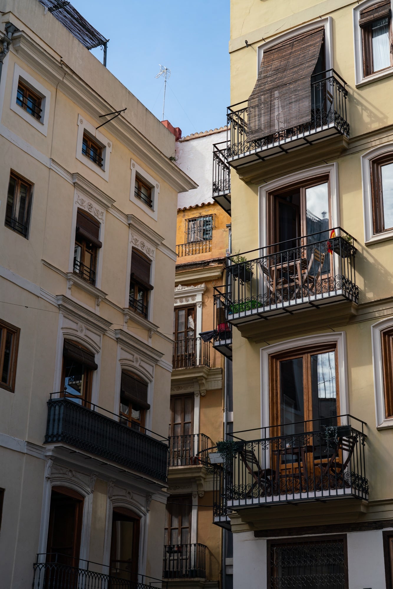 Looking up between cream townhouses hung with iron balconies and wooden blinds toward a sliver of blue sky