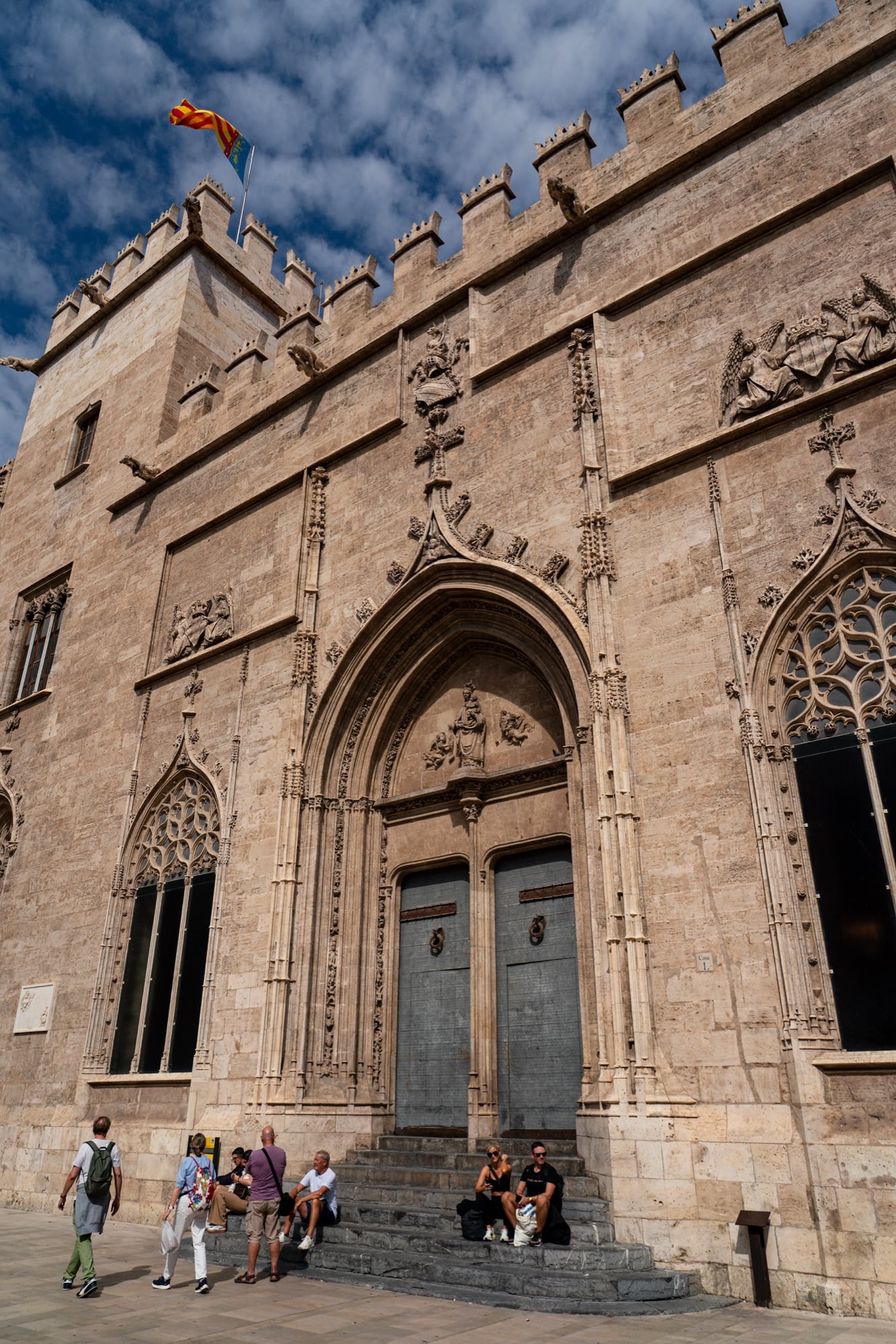 The Gothic portal of La Lonja de la Seda, visitors resting on its stone steps below the battlements