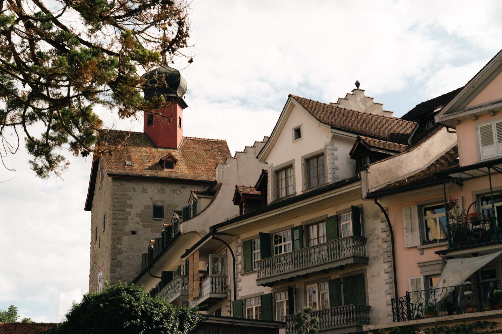 Old-town rooftops and balconies climbing the hillside beside a stone tower topped with a red onion-domed turret