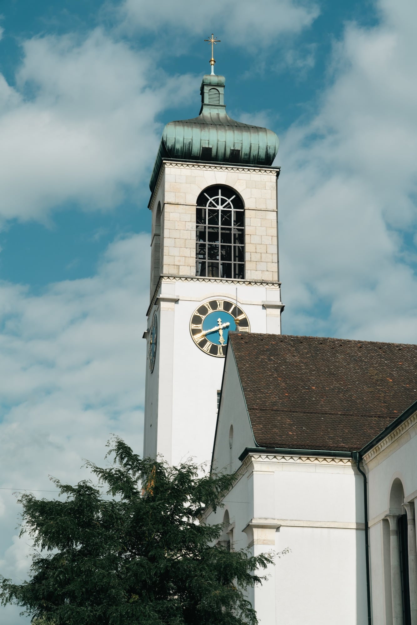 The white parish church tower of Appenzell with its green onion dome and gold clock against a blue sky