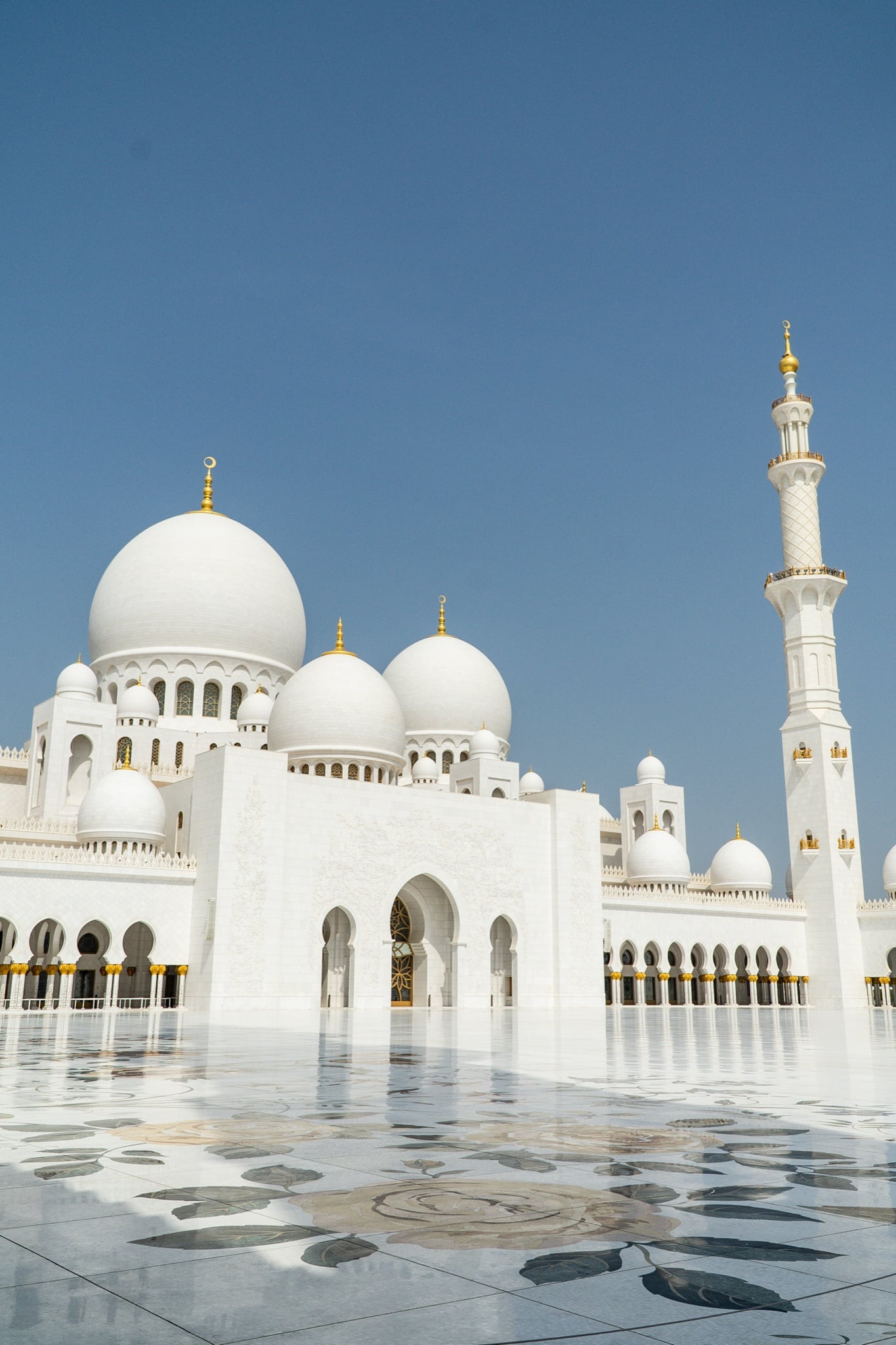 The white marble domes and gold-tipped minaret of the Sheikh Zayed Grand Mosque above its reflecting courtyard