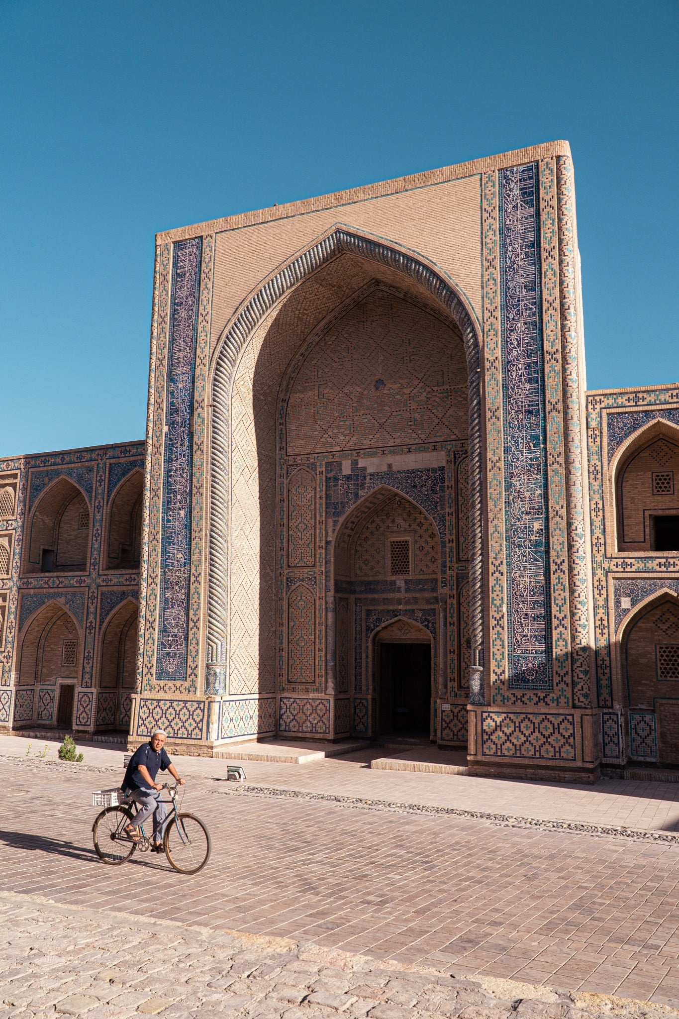 A man cycling past a weathered building in old Bukhara